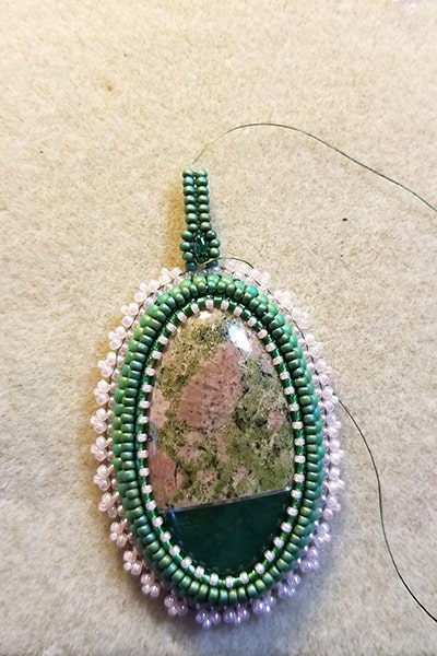 Stone cabochon with several layers of beadingg creating a bezel and bail in green and pink.