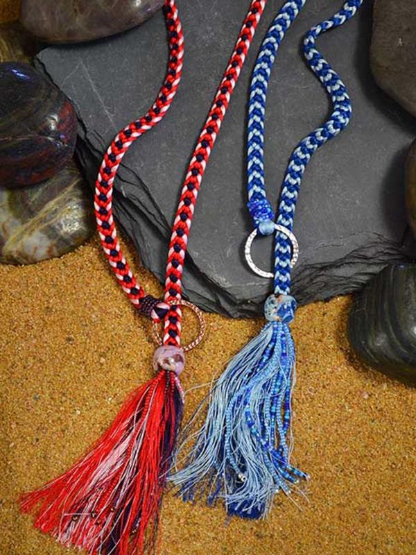 Flat kumihimo braids in red and blue with multicolored bead and fringe