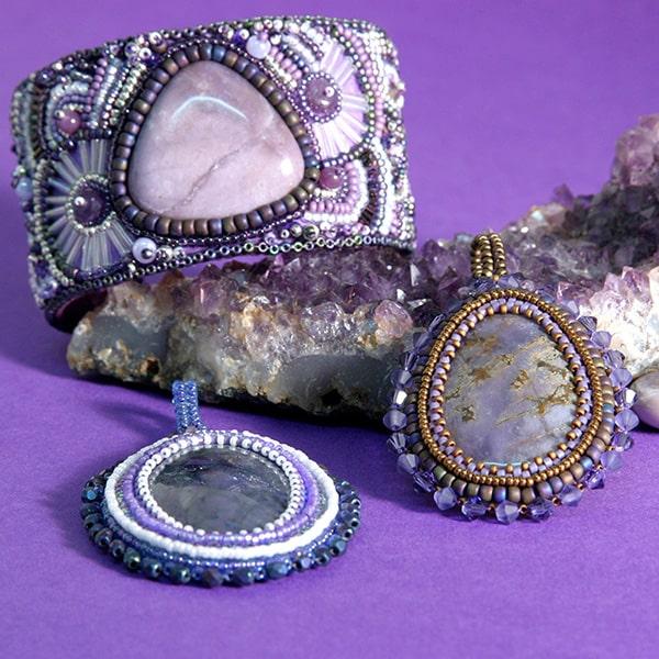 Grouping of purple bead embroidered jewelry pieces: a large cuff, and two pendants on a beautiful piece of Amethyst geode